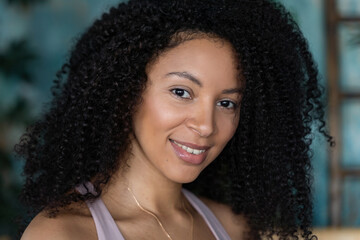 Middle-aged curly Brazilian woman posing over painted green plant blue background. Looking at camera.