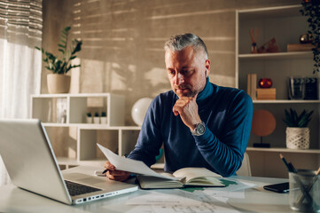 Middle aged man working in a home office and using laptop and paper documents