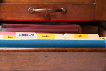 File folders with insurance, auto, health, and life tabs in an antique file drawer.