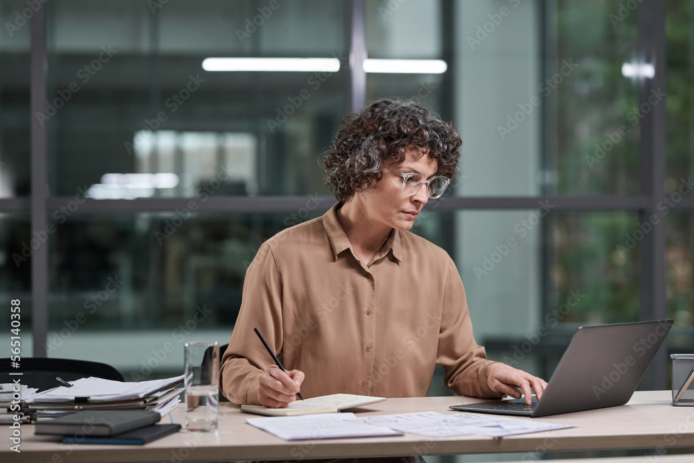 Poster experienced female broker in beige blouse working over business project while sitting by workplace i