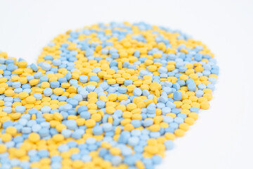 Pills of yellow and blue color in the form of a heart on a white background. Medicine, treatment, pharmacology, health. Top view Close up Mosaic