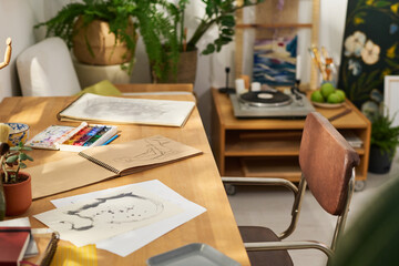 Papers and notepad with sketches drawn by artist in home studio with table, chair, green plants,...