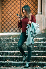 Attractive young woman standing at the city stairs and using a smartphone.
