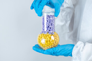 Doctor in protective latex blue gloves on a white background holds glass flask with yellow and blue pills Medical Treatment Health Choice of pills Space for text