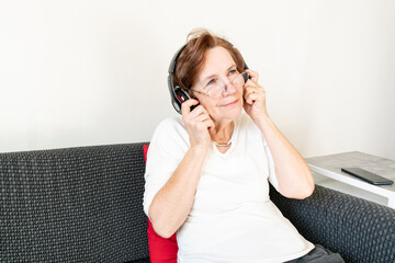 old senior woman female sit home flat couch listen music headphones happy smile relax enjoy