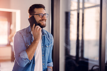 Handsome young man with glasses standing in the office and using the phone.