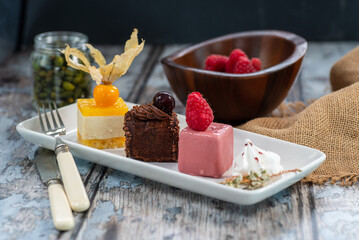 set of cakes, tangerine, chocolate and raspberry flavors, with physalis and strawberry raspberries, on white rectangular plate, worn wooden background in blue tones. diebates concept,