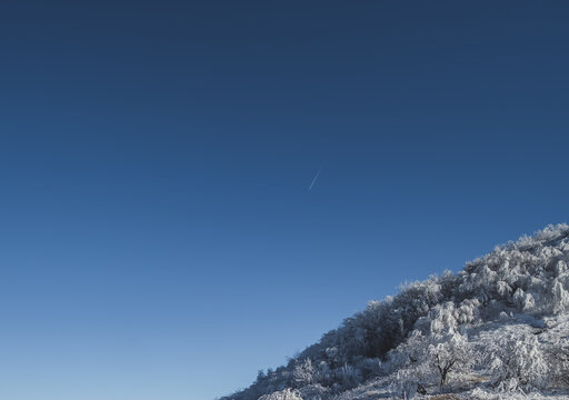 Winter panorama, the slope of Mount Beshtau with icy and snow-covered vegetation against a clear blue sky, a condensation trail from an airplane in the sky on a sunny winter day - Powered by Adobe