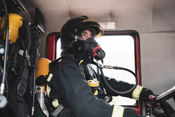 Profile view. A firefighter is sitting in the back of a uniformed fire truck wearing a gas mask...