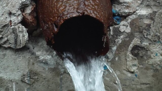 Clean water for drinking and food flows out of a rusty metal pipe, close-up