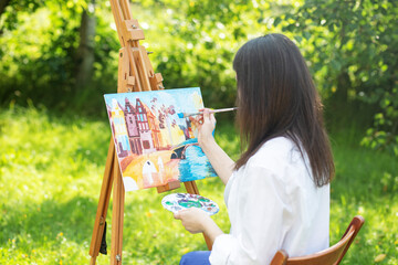Young female artist paints picture in summer park in sunlight. Art and hobby concept.