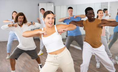 Group of energetic different people learning dance at dance class