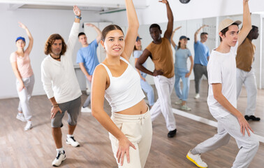 Group of young adult active multiethnic dancers stretching one arm up during learning new dance exercise movement in gym - obrazy, fototapety, plakaty
