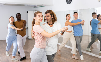 Smiling dancing people practicing movements while dancing in pairs in dance school for adults