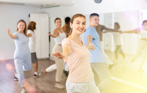 Smiling young adult couples dancing together in pairs and practicing movements in modern choreography class