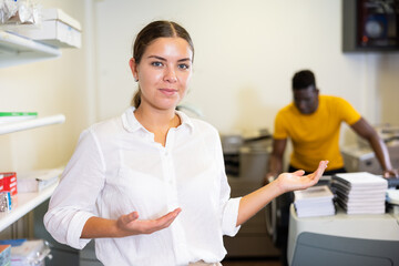 Happy young woman in white shirt sticking out her left hand to show the workflow in the printing...