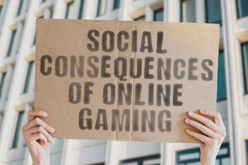 The phrase " Social consequences of online gaming " is on a banner in men's hands with blurred background. Young. Competition. Enjoyment. Professional. Video Game. Cyberspace. Sitting. Modern. Digital
