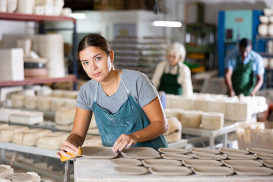 Young caucasian woman potter in apron polishing new crafted plates with sponge. © JackF