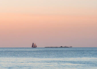 Obraz premium a schooner sails on the horizon as the sun sets with an orange glow over the lake on a summer evening