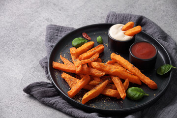 Sweet potato sticks in a black plate served with mayonnaise and ketchup sauce.