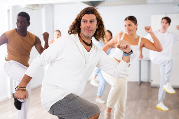 Group of excited young adult diverse dancers performing dynamic movements during training together in fitness studio