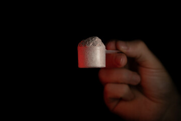 Closeup view of a male hand holding a scoop of powder with red accent lighting