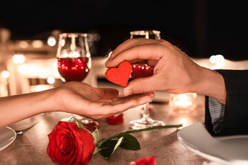 Romantic candle light Valentine's dinner setting. Man giving woman a heart gift of love.