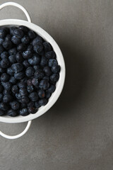 Fresh Picked Blueberries in a white colander on gray slate with copy space. Only half the colander is shown.