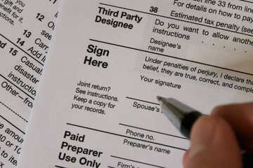 A hand is shown just before before signing an Internal Revenue Service IRS form 1040 in the USA, shown up close.