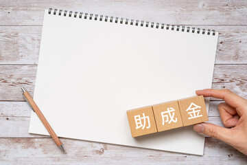 助成金と書かれたブロック、ノート、ペン、手