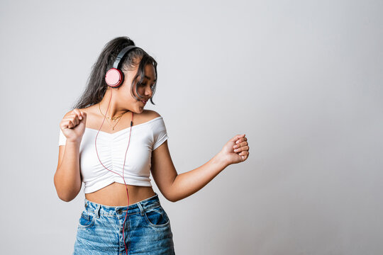 Latin girl listening to music, dancing and having fun. Teenager using a music app. Latin American person enjoying the rhythm. Advertising image with neutral background