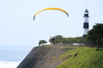 Fototapeta na wymiar Paragliding is action sport in Lima Peru. Person is paragliding in Miraflores Lima Peru with lighthouse and buildings background.. Selective focus. Open space area. 