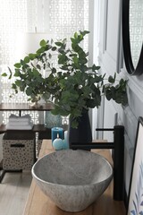 Eucalyptus branches near vessel sink on bathroom vanity. Interior design