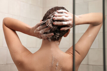 Woman washing hair while taking shower at home, back view