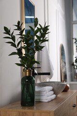 Eucalyptus branches and folded towels near stylish vessel sink on bathroom vanity. Interior design