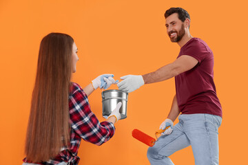 Man taking can of paint from woman near orange wall. Interior design