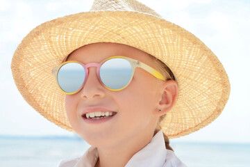 Little girl wearing sunglasses and hat at beach on sunny day