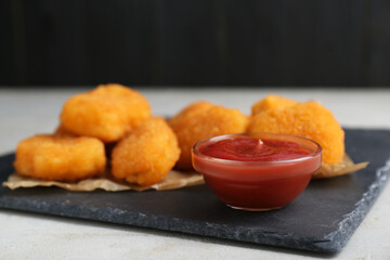 Tasty chicken nuggets with ketchup on light grey textured table, closeup