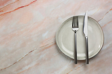 Clean plate and cutlery on beige marble table, top view. Space for text