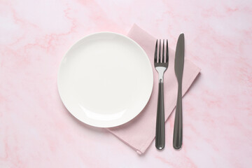 Fototapeta na wymiar Clean plate and shiny silver cutlery on light pink marble table, flat lay