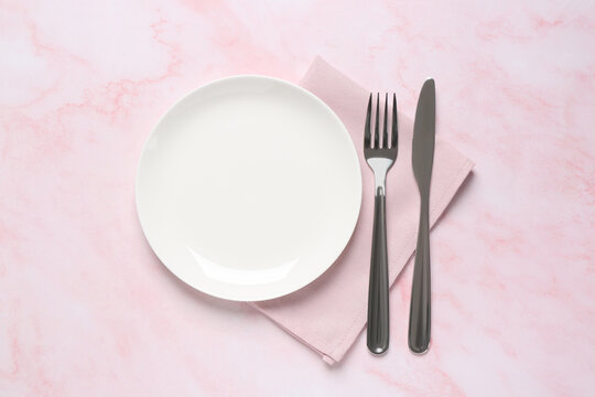 Clean plate and shiny silver cutlery on light pink marble table, flat lay