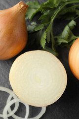 Whole and cut onions with parsley on black textured table, flat lay