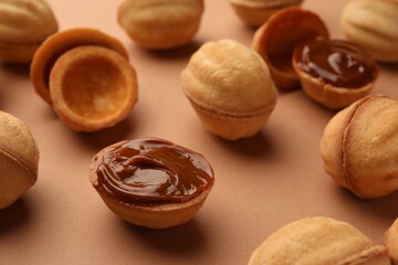 Homemade walnut shaped cookies with boiled condensed milk on pale brown background, closeup