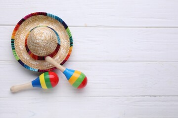 Colorful maracas and sombrero hat on white wooden table, flat lay with space for text. Musical instrument