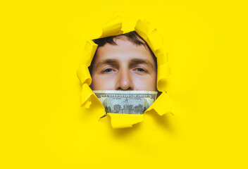 The man's face pokes out through a torn hole in the yellow paper, with a hundred dollar bill and a...