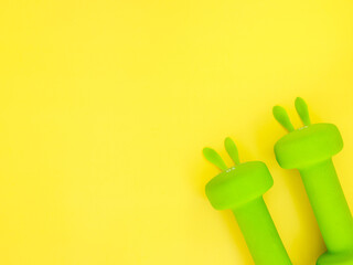 two green heavy dumbbells with leaves in shape of Easter bunny on yellow background. Easter fitness...