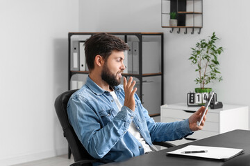 Handsome young businessman video chatting with tablet computer at table in office