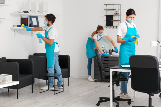 Young janitors with medical masks cleaning in office