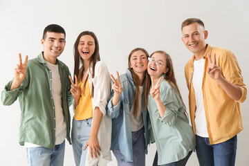 Group of happy friends showing victory gesture on light background