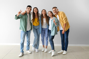 Group of happy friends showing victory gesture near light wall
